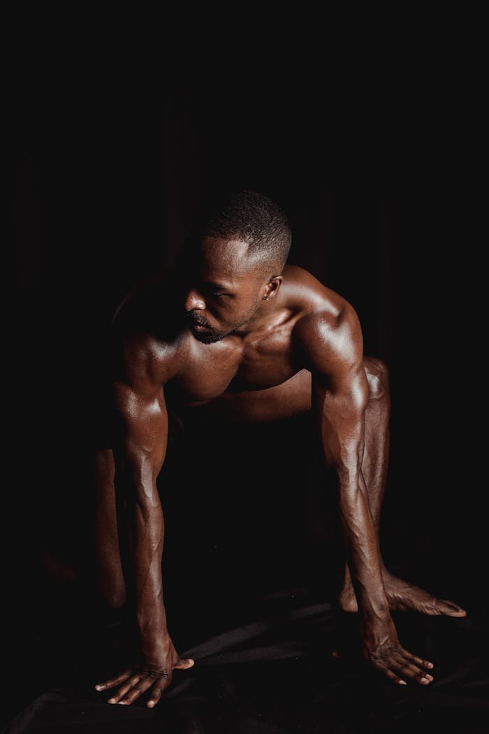 About African American muscular man posing with strength against a dark backdrop.
